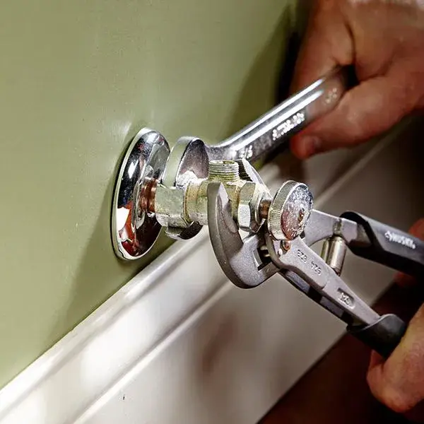Plumber replacing a chrome shut-off valve with a wrench