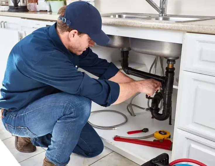 Plumber repairing pipes under a kitchen sink in a Gilbert home